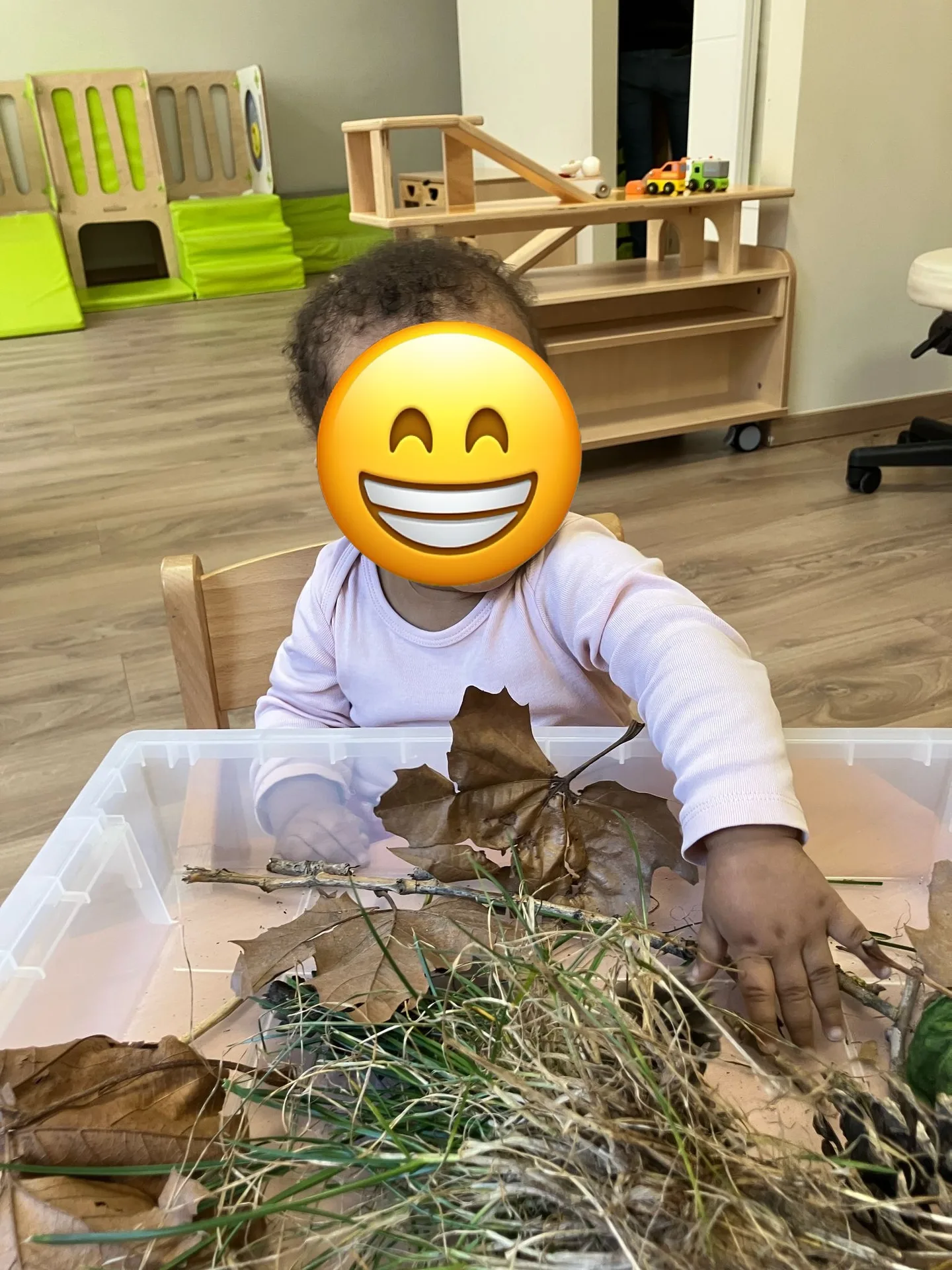 Bébé souriant explore un bac sensoriel de feuilles et branches à la crèche de Differdange