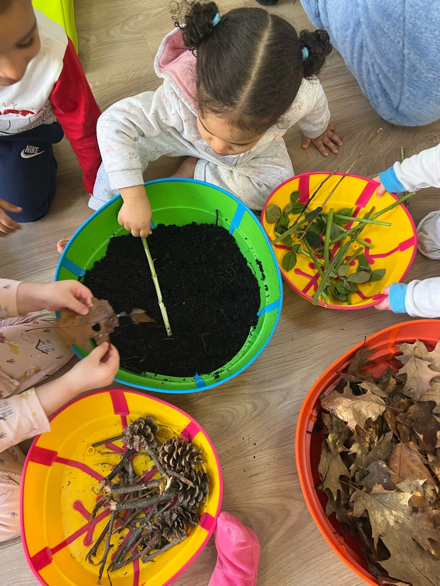 Atelier nature avec bassines de terre, feuilles, pommes de pin et branches à Differdange