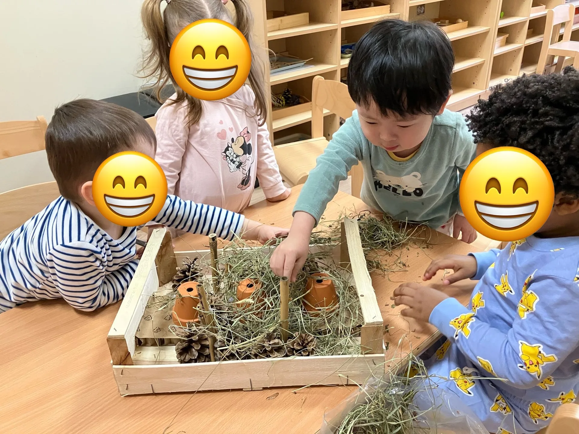 Groupe d'enfants autour d'un jardin miniature avec foin, pommes de pin et pots en terre