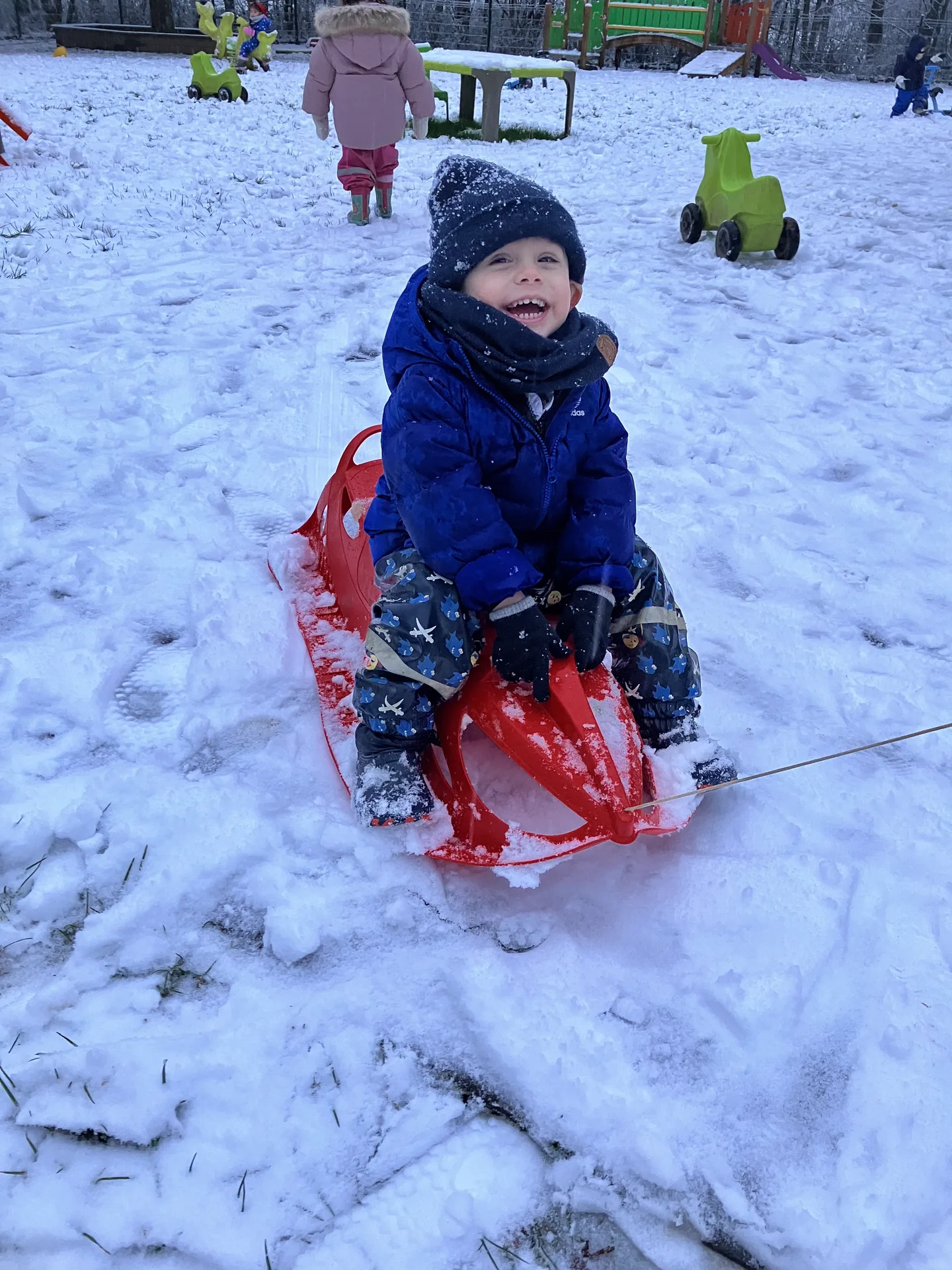Enfant heureux sur sa luge rouge, activité hivernale à la crèche de Kockelscheuer