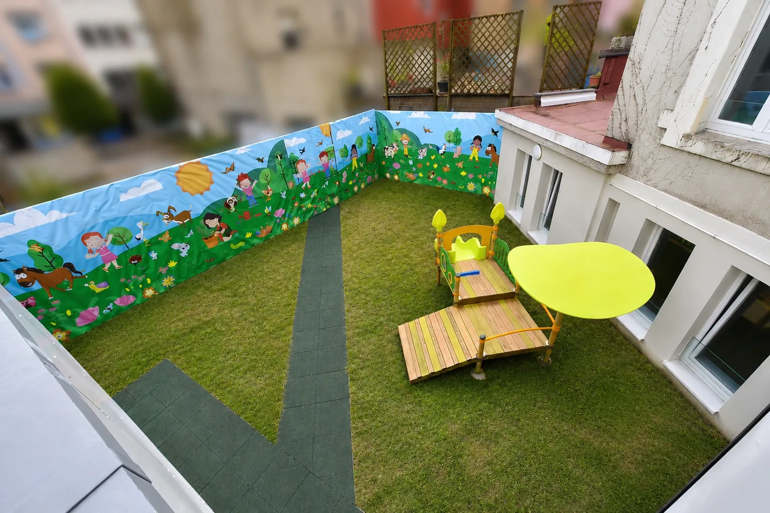 Terrasse extérieure sécurisée avec gazon synthétique et fresque colorée à la crèche de Differdange