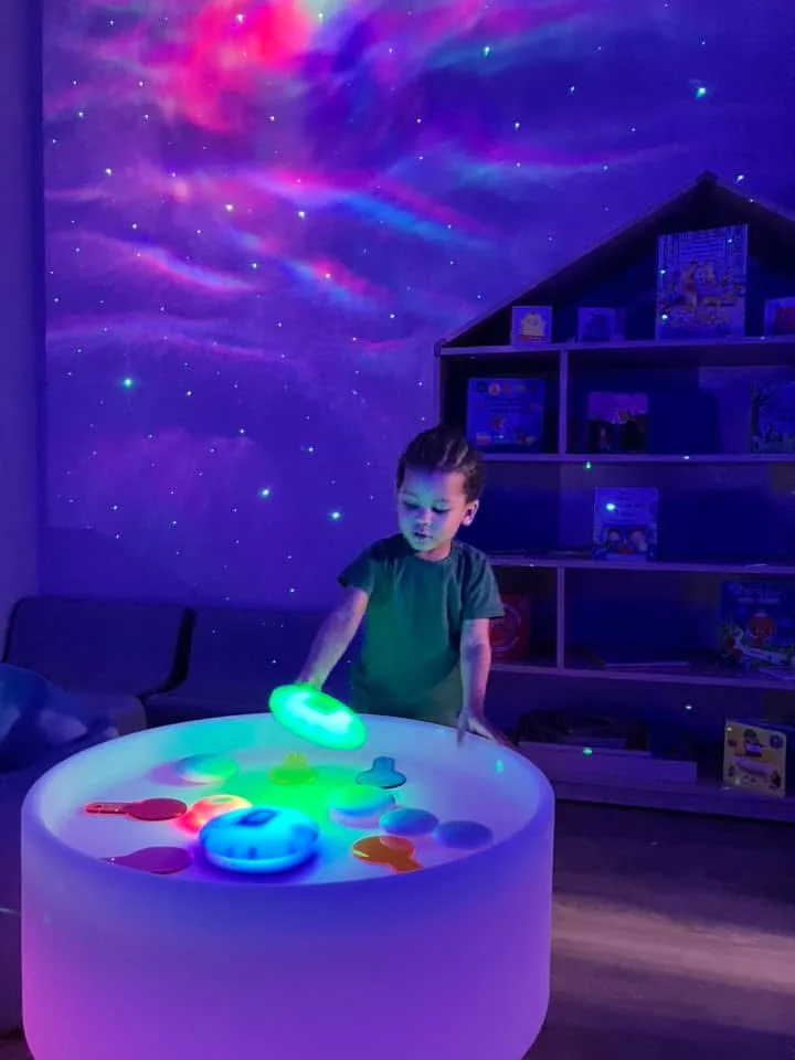 Enfant émerveillé devant la table lumineuse dans la salle Snoezelen de la crèche de Differdange
