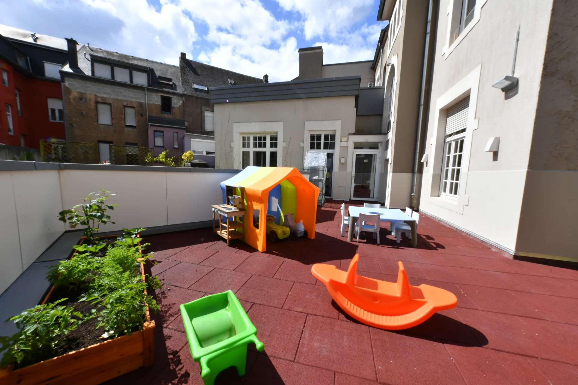 Terrasse ensoleillée avec cabane, bascule et carrés potagers à la crèche de Differdange