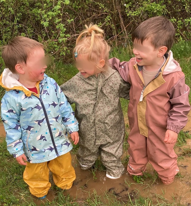 Trois enfants heureux jouant dans une flaque de boue en tenue de pluie à la crèche nature Schnick Schnack Schnuck