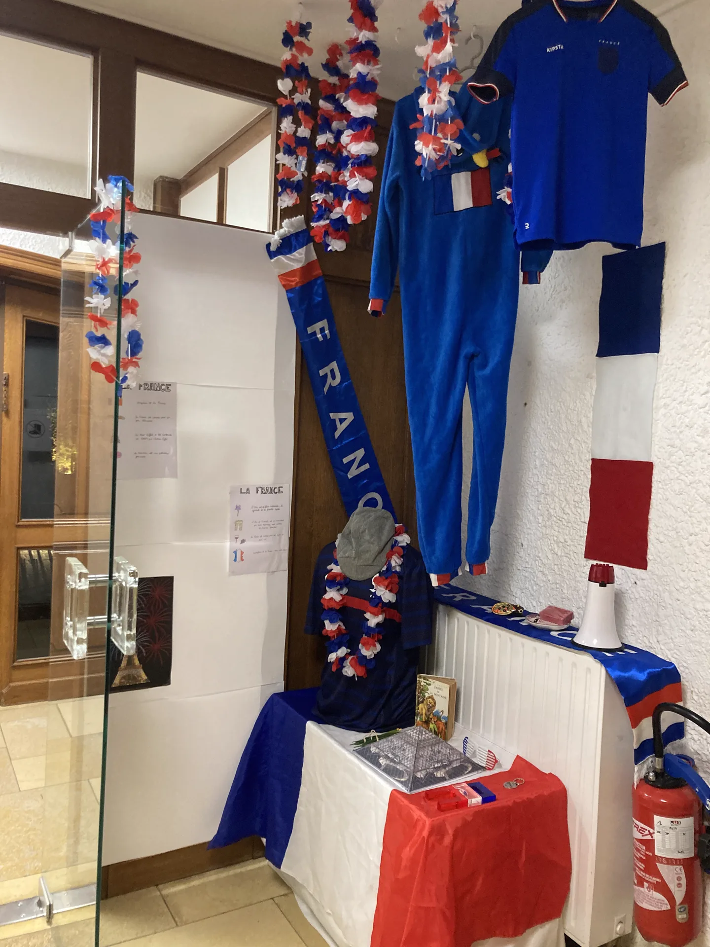 Coin découverte de la France : maillot bleu, écharpe et guirlandes tricolores dans le hall de la crèche