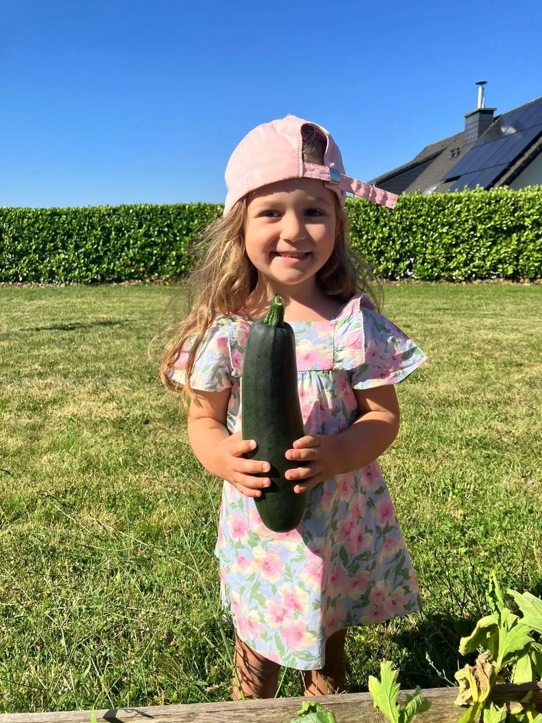 Enfant tout sourire qui tient fièrement une grosse courgette récoltée au potager