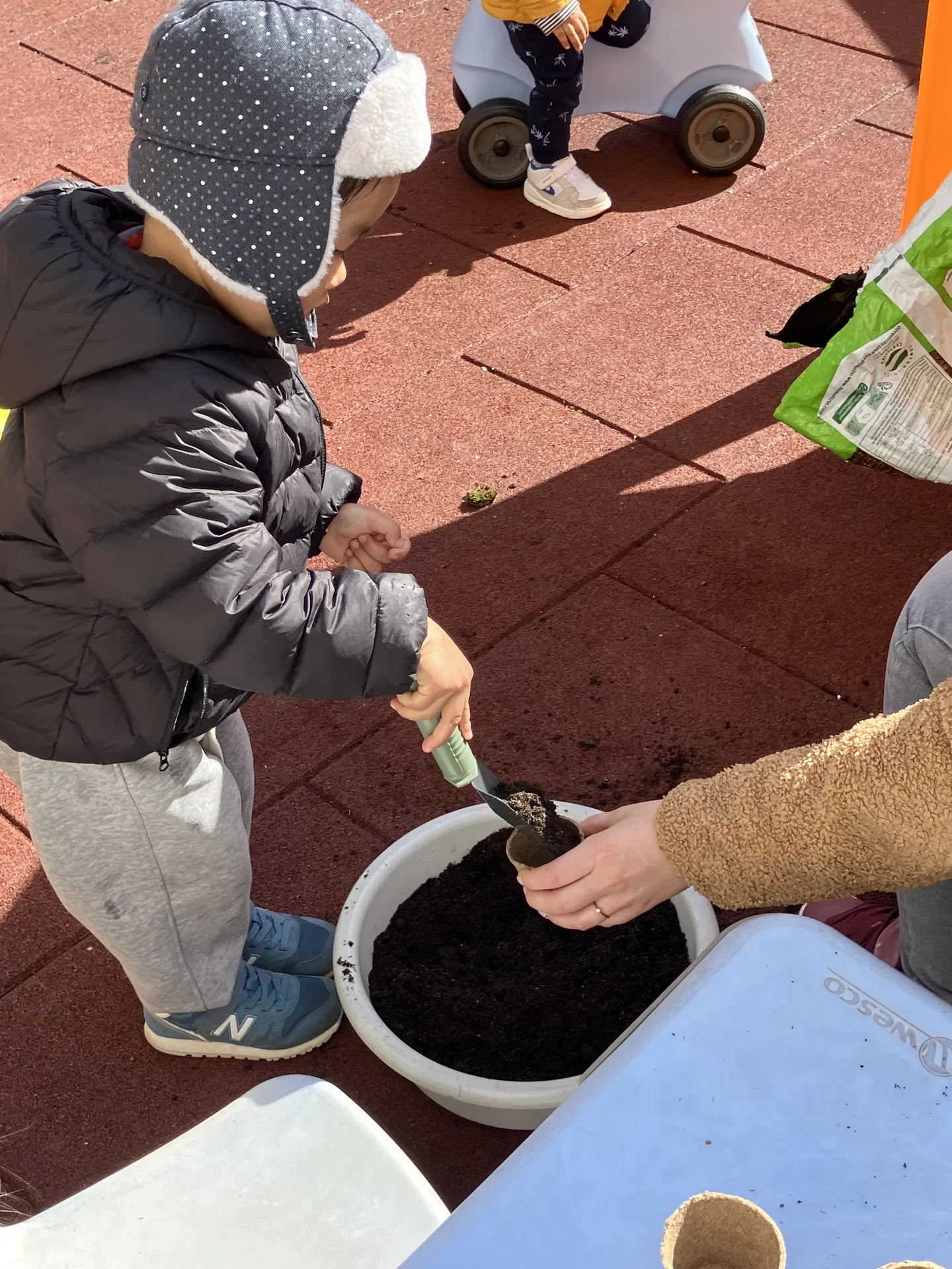 Remplissage des godets biodégradables avec du terreau, atelier jardinage à la crèche